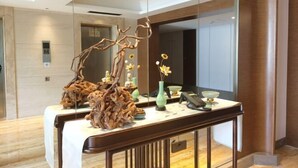 Un mostrador de recepción con un espejo, un teléfono y elementos decorativos, incluyendo un florero con flores y una escultura de una rama de árbol.