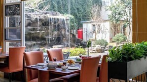 Un área de comedor al aire libre con vista a una cascada, sillas naranjas y una mesa de comedor con platos, vasos y un jarrón de flores.