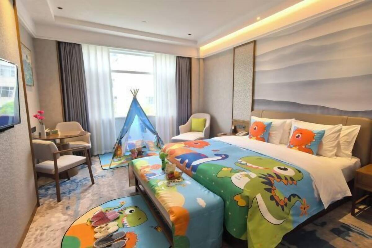 A hotel room with a bed, a desk, a chair, a small table, a window with curtains, and a tent-like structure.
