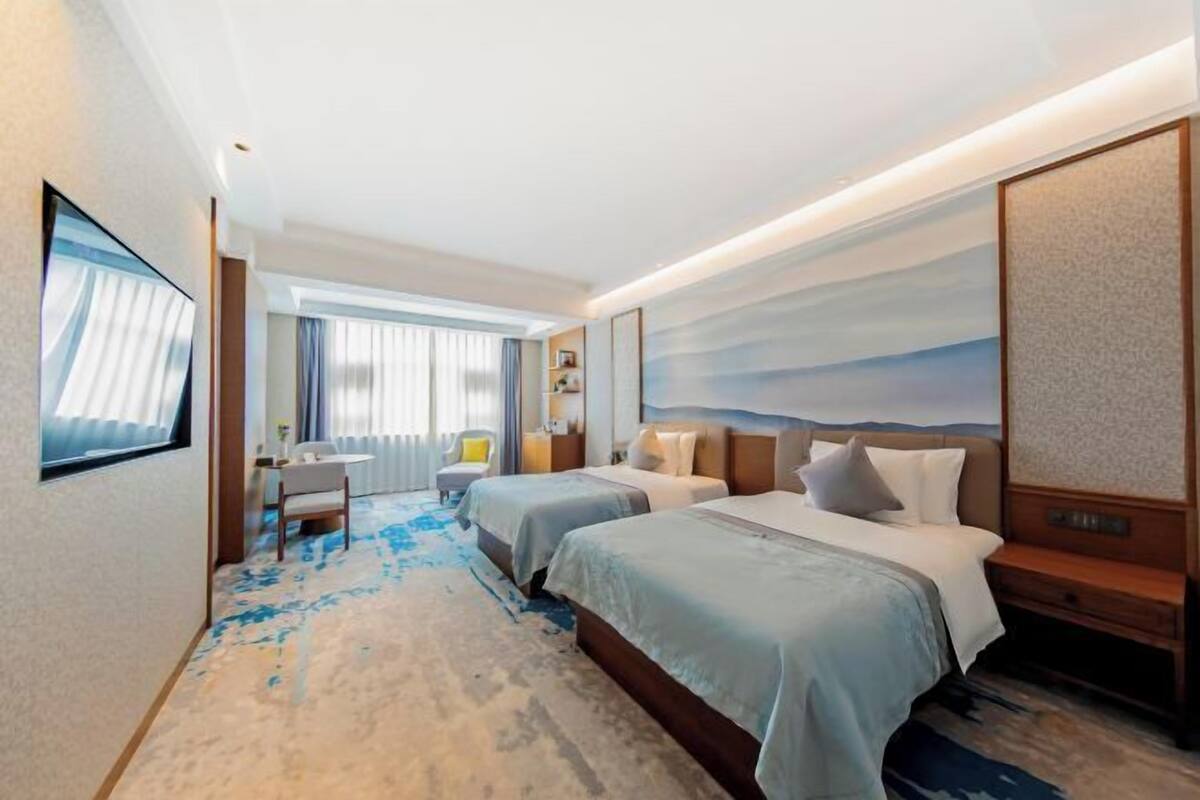 A hotel room with two beds, a desk, a chair, and a large window with curtains.