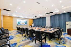 A conference room with a long table, chairs, a projector screen, and a blue curtain backdrop. - NEW OVERSEAS CHINESE HOTEL (Zhoushan)