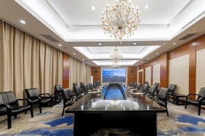 Une salle de conférence avec une longue table, des chaises, un lustre et un grand écran.