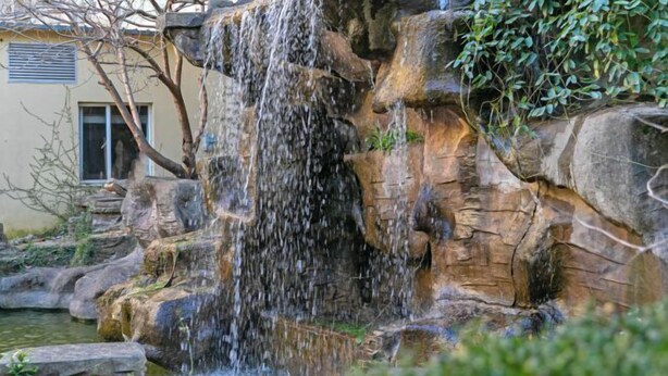 Una cascada se precipita sobre terreno rocoso, con un edificio al fondo.