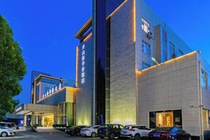 Een modern hotelgebouw met een opvallende ingang, diverse parkeerplaatsen en een goed verlichte gevel.