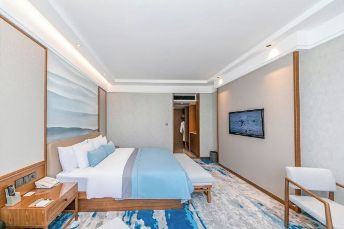 Habitación de hotel con una cama grande, una mesita de noche, una silla y un cuadro en la pared.