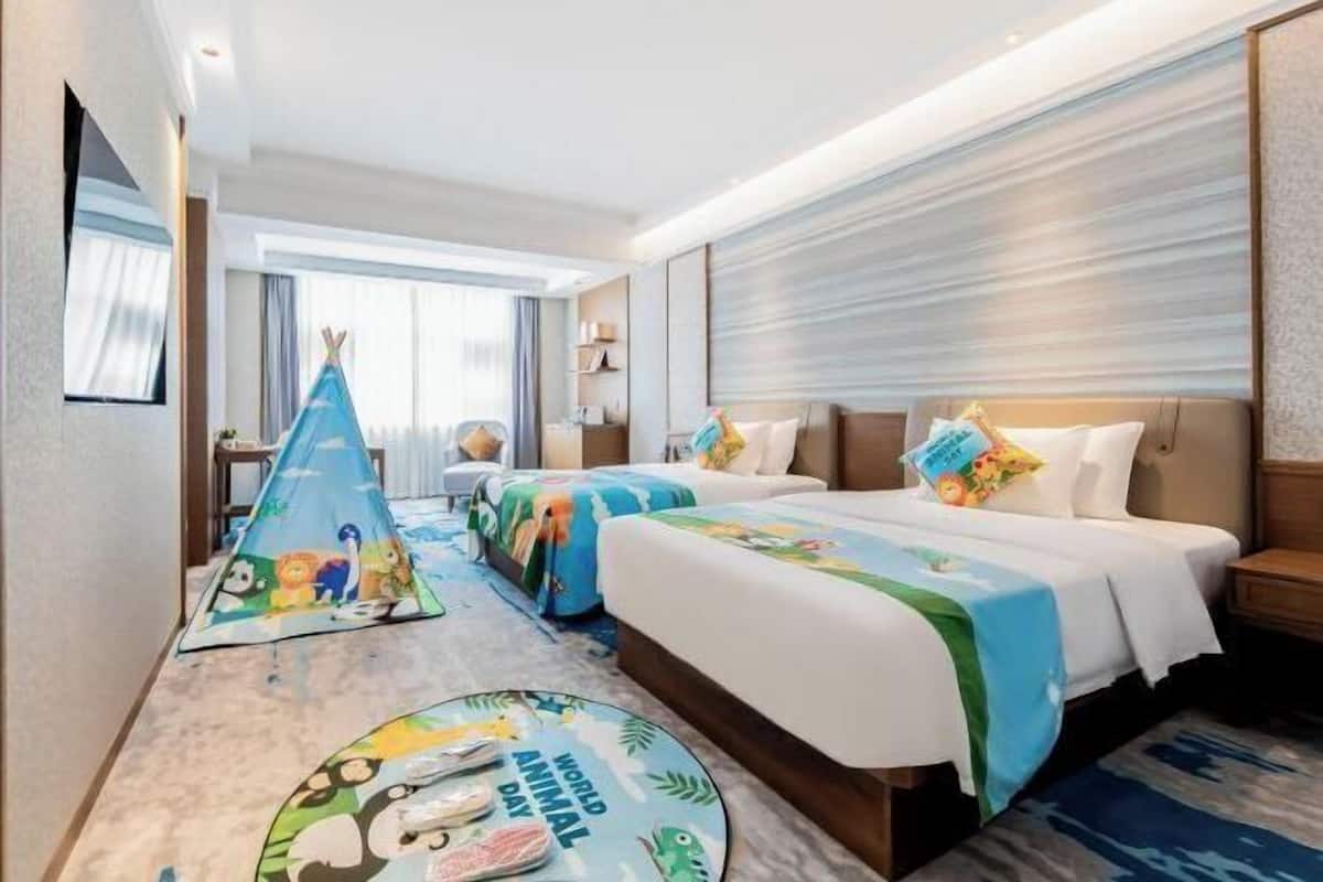 A hotel room with two beds, a small table, a chair, and a window.