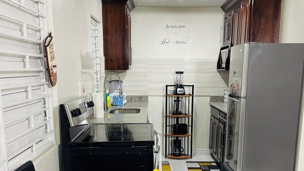 Una cocina moderna con estufa negra, refrigerador de acero inoxidable y una cafetera. Hay una mesa de comedor con platos, cubiertos y servilletas.