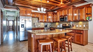 A kitchen with wooden cabinets, granite countertops, and a central island with stools. - Hol Chan Ocean Front Residences (San Pedro)