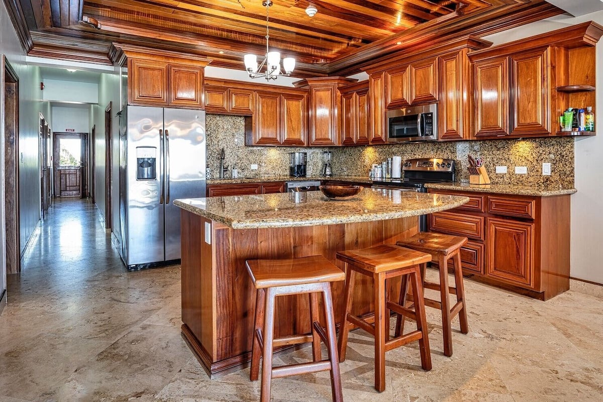 A kitchen with wooden cabinets, granite countertops, and a central island with stools.