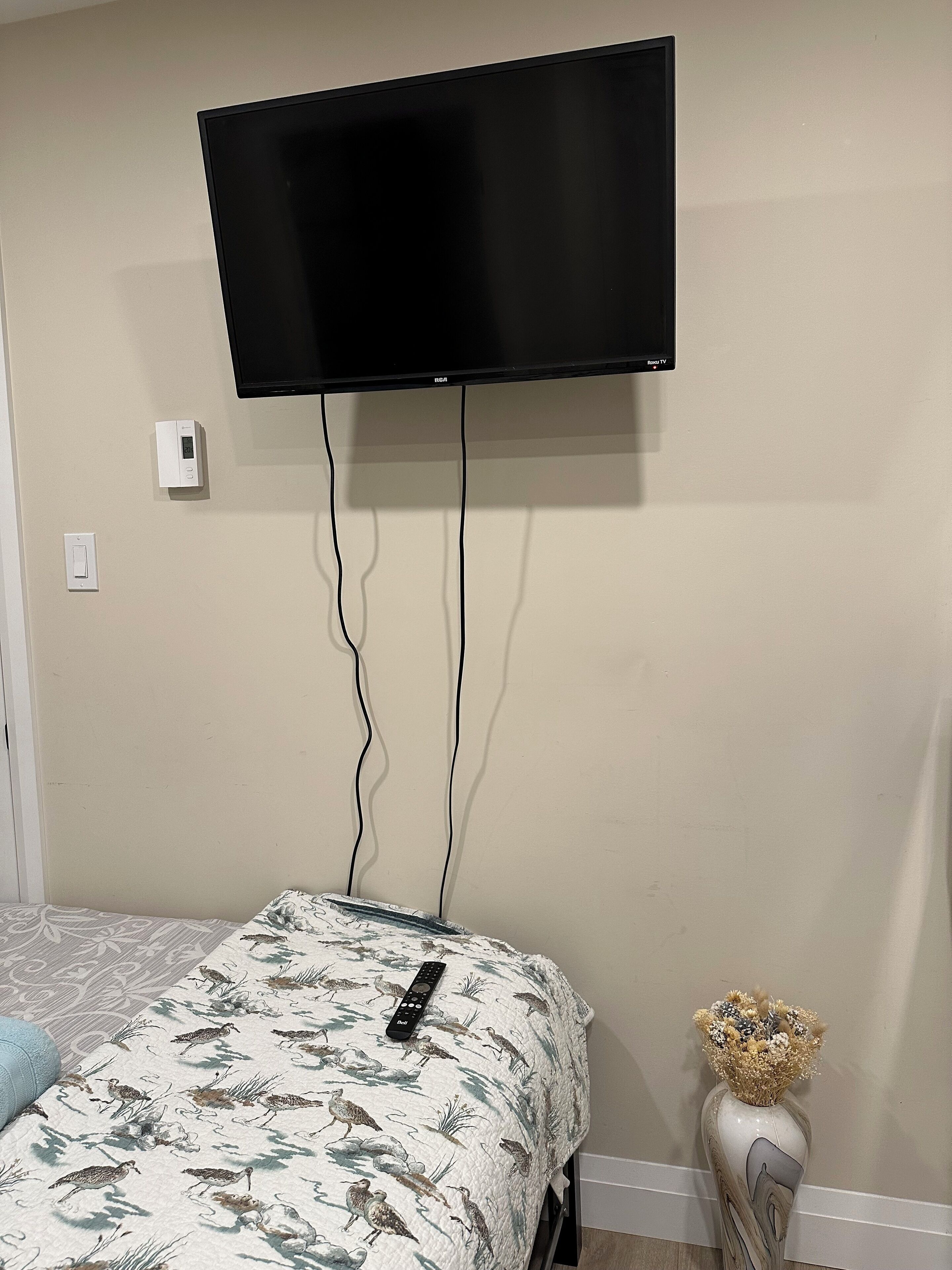 A bedroom with a bed, a mounted TV, and a remote control on the bed.