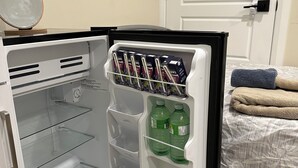 A small, white refrigerator with a freezer compartment on the left and a main compartment on the right. Inside the freezer, there are several boxes of a beverage, and the main compartment contains two large bottles of water. - Charming small studio in adorable St. John's WiFi access, 2 twin beds, full bath (St. John's)