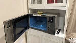A microwave with a digital display, a remote control, and a small bowl on top. - Charming small studio in adorable St. John's WiFi access, 2 twin beds, full bath (St. John's)