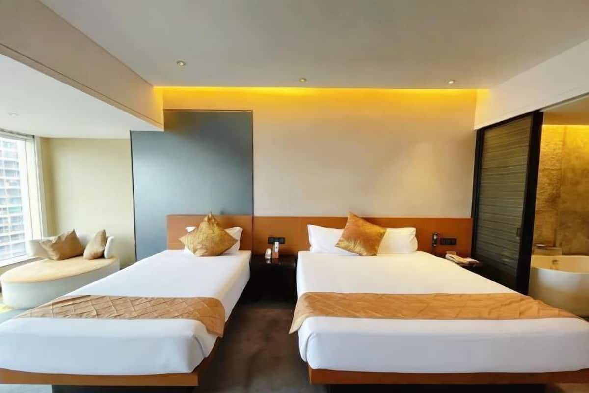 A hotel room with two beds, a sofa, a large mirror, a window, and a bathroom.