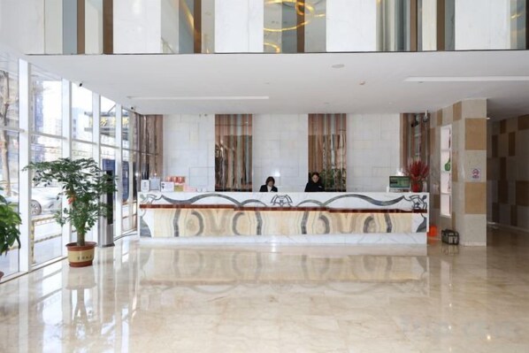 Zona de recepción de un hotel con mostrador de mármol, amplias ventanas y una planta en maceta.