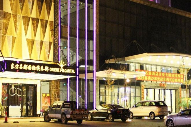 Un edificio con fachada moderna, señalización iluminada y vehículos estacionados al frente.