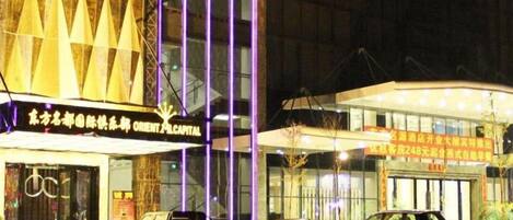 A building with a modern facade, illuminated signage, and parked vehicles in front.