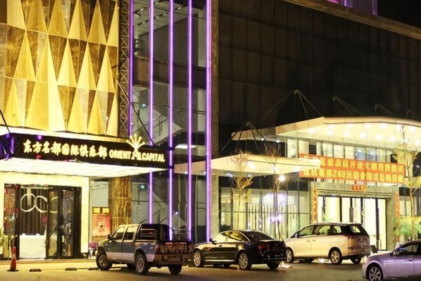 A hotel with a modern facade, multiple vehicles parked in front, and illuminated signage. - Dongfang Mingyuan Hotel (Longchuan)