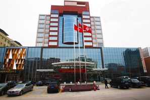 Een modern hotel met een opvallende rode vlag op de gevel, een glazen ingang en een parkeerplaats met meerdere auto's.