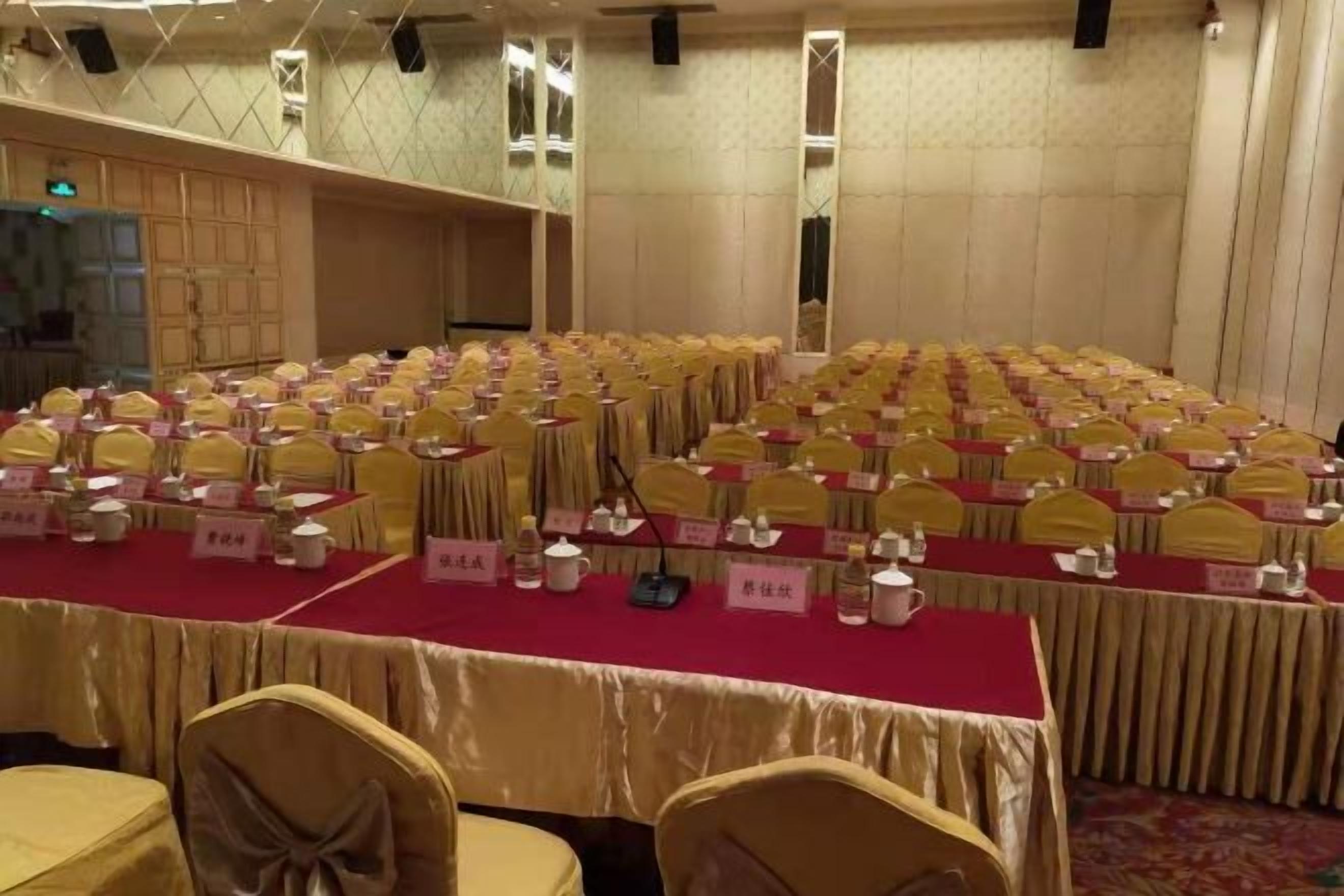 A banquet hall with rows of tables and chairs, nameplates, and microphones.