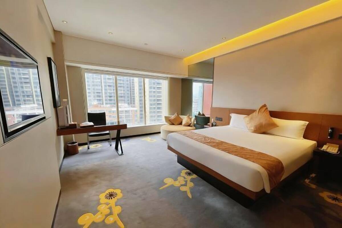 A hotel room with a large bed, a desk, a chair, and a window with a city view.