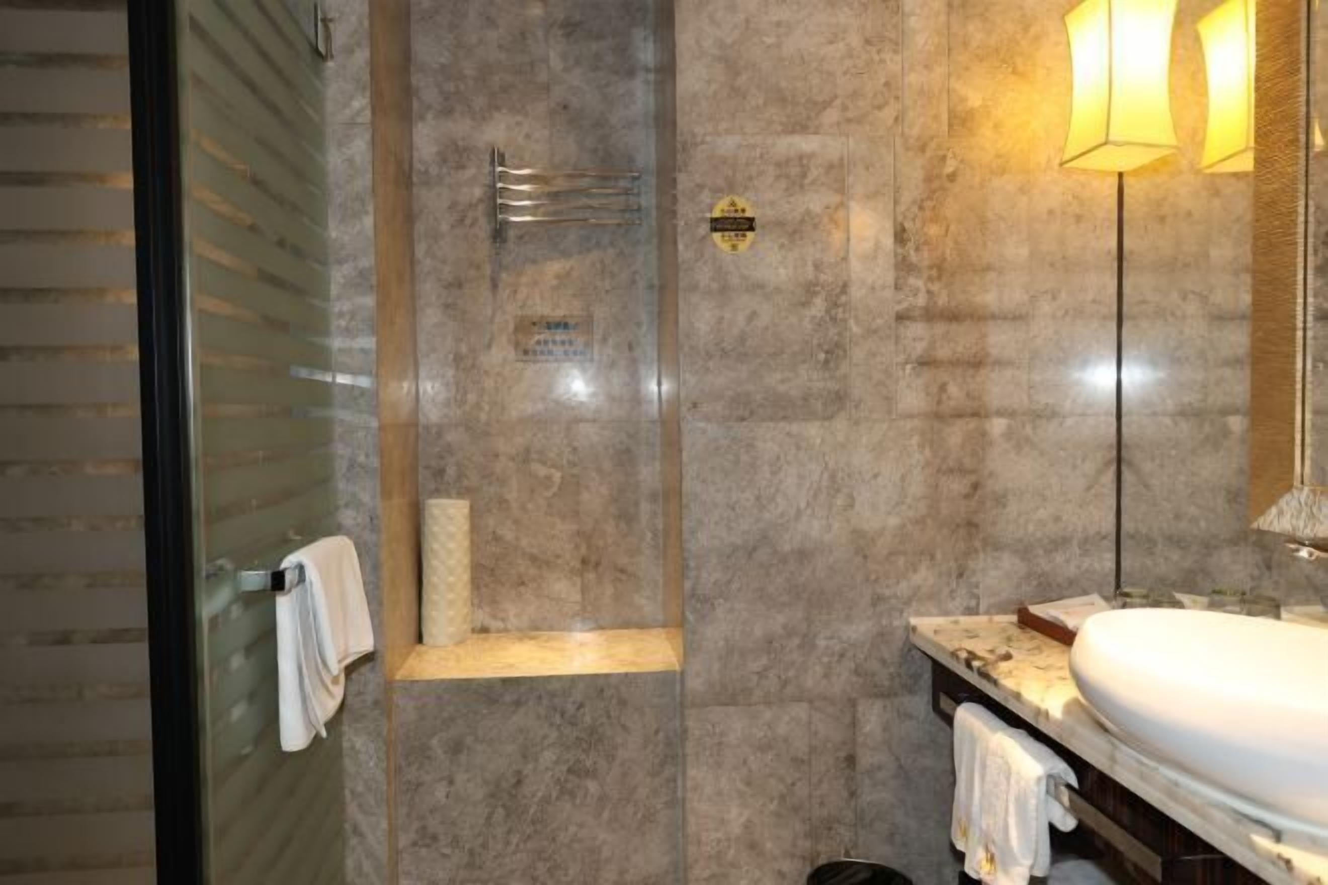 Un baño moderno con cabina de ducha de vidrio, pared revestida de mármol, lavamanos con espejo y un perchero para toallas.
