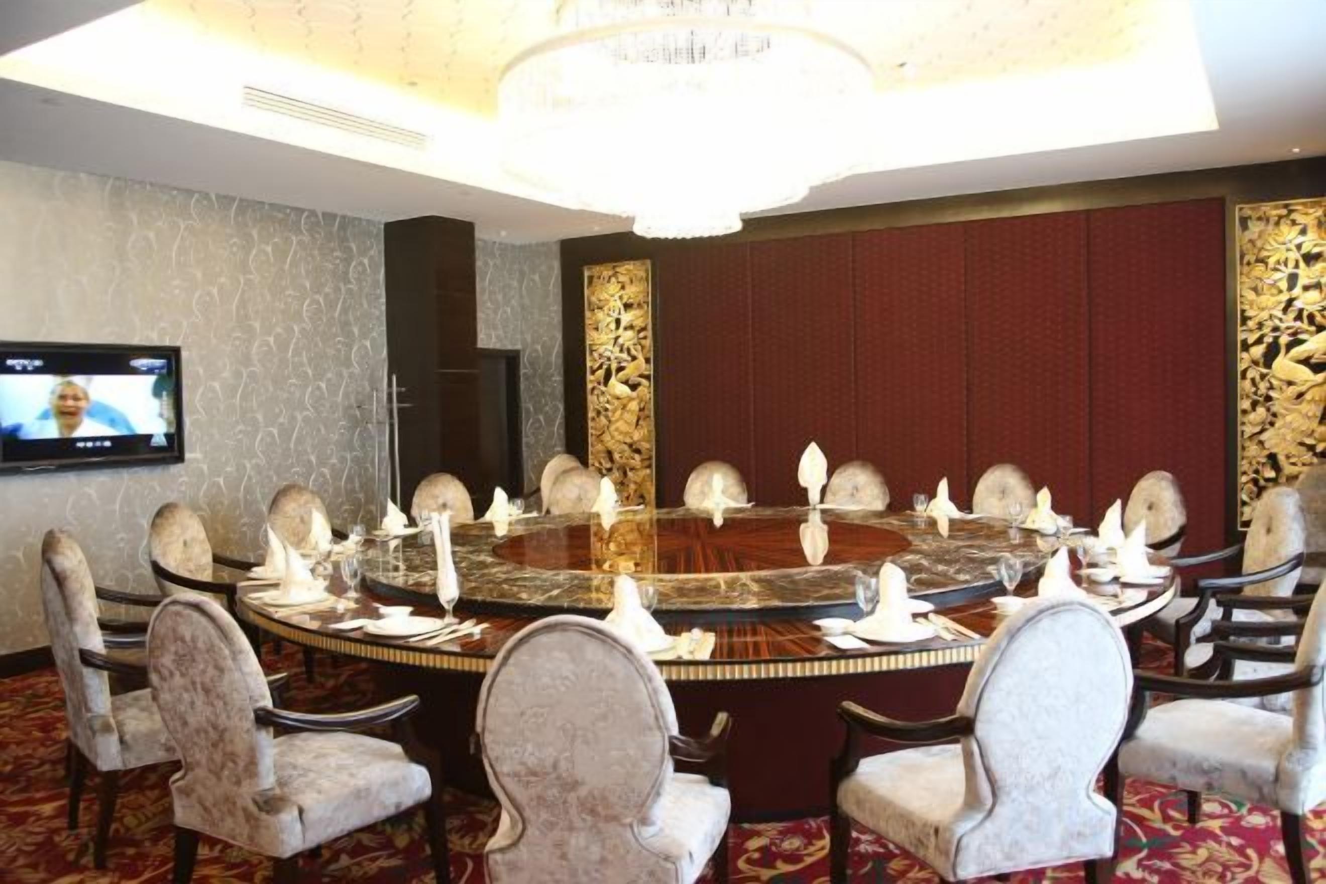 Un salón de conferencias con una mesa redonda, sillas, una televisión y una araña.