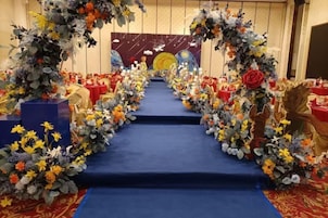 A stage with a blue carpet, surrounded by floral arrangements and red tables.