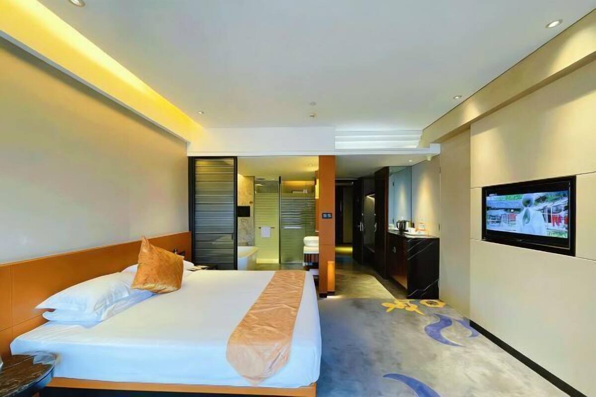A hotel room with a bed, a TV, and a hallway leading to a bathroom.