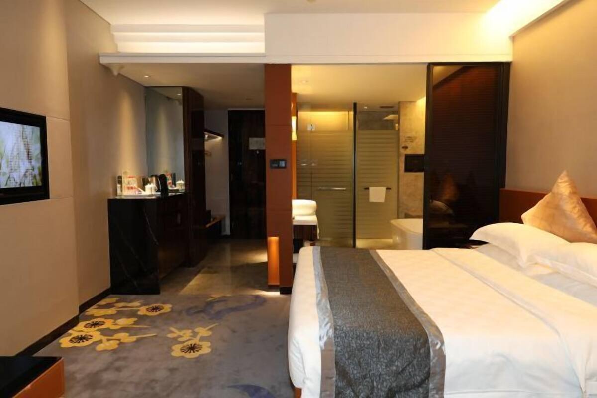 A hotel room with a bed, a desk, a chair, a mirror, and a bathroom with a shower.