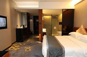A hotel room with a bed, a desk, a chair, a mirror, and a bathroom with a shower.