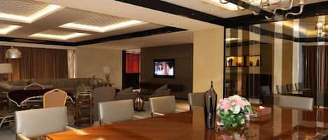 Un salón de conferencias moderno en un hotel, con una gran mesa de madera, asientos cómodos, una televisión e iluminación ambiental.