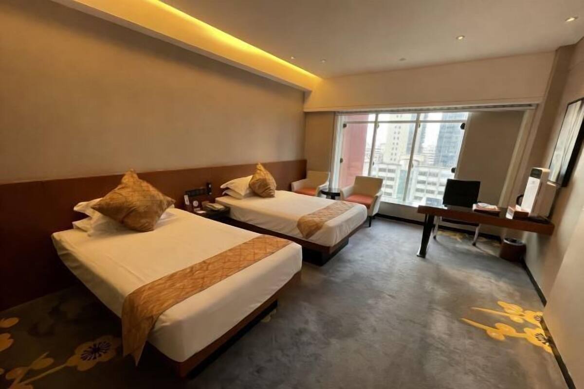 A hotel room with two beds, a desk, a chair, a television, and a large window with a city view.