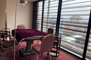 A room with a dining table, chairs, a window with blinds, and a view of buildings. - Dongfang Mingyuan Hotel (Longchuan)