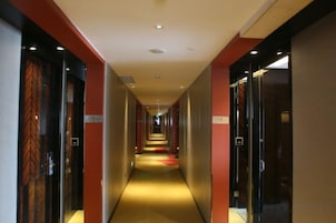 Un pasillo de hotel con puertas a ambos lados, suelo alfombrado y una alfombra roja que conduce al final.