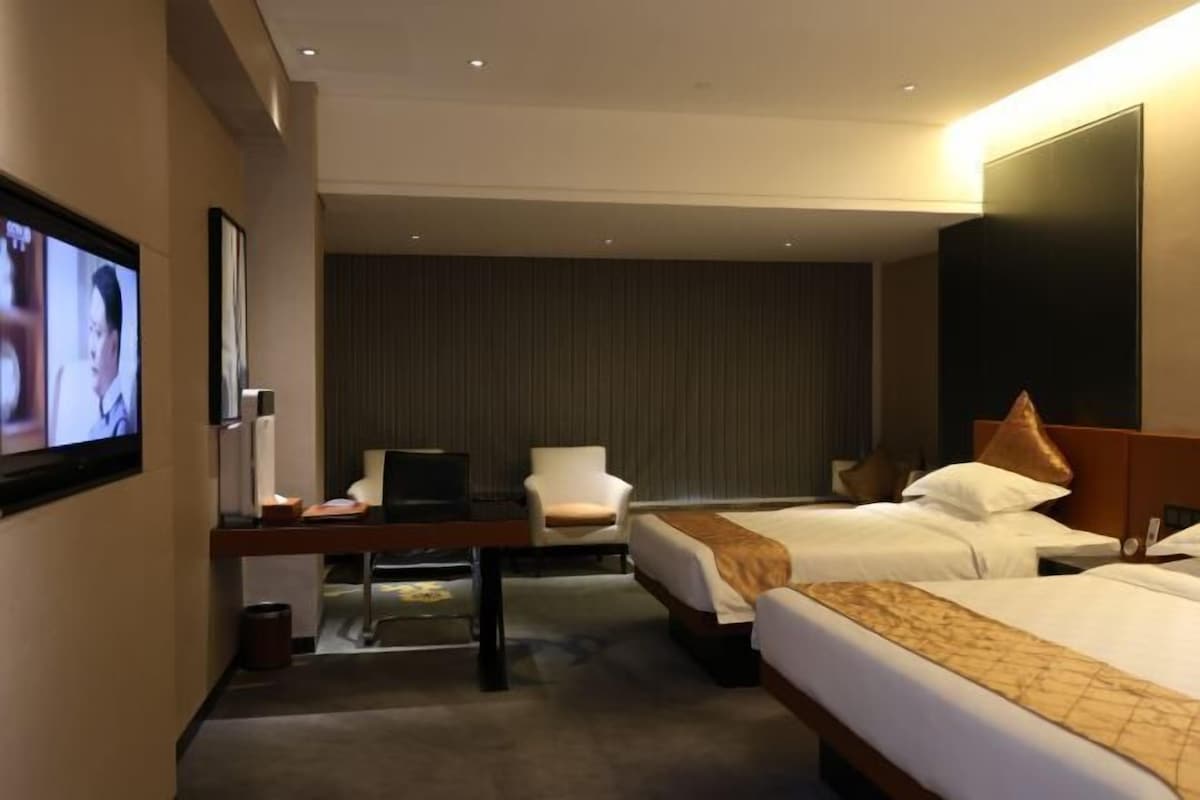 A hotel room with two beds, a desk with a chair, a TV, and a large wall-mounted TV.