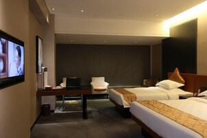 Habitación de hotel con dos camas, un escritorio con silla, televisor y un televisor grande montado en la pared.