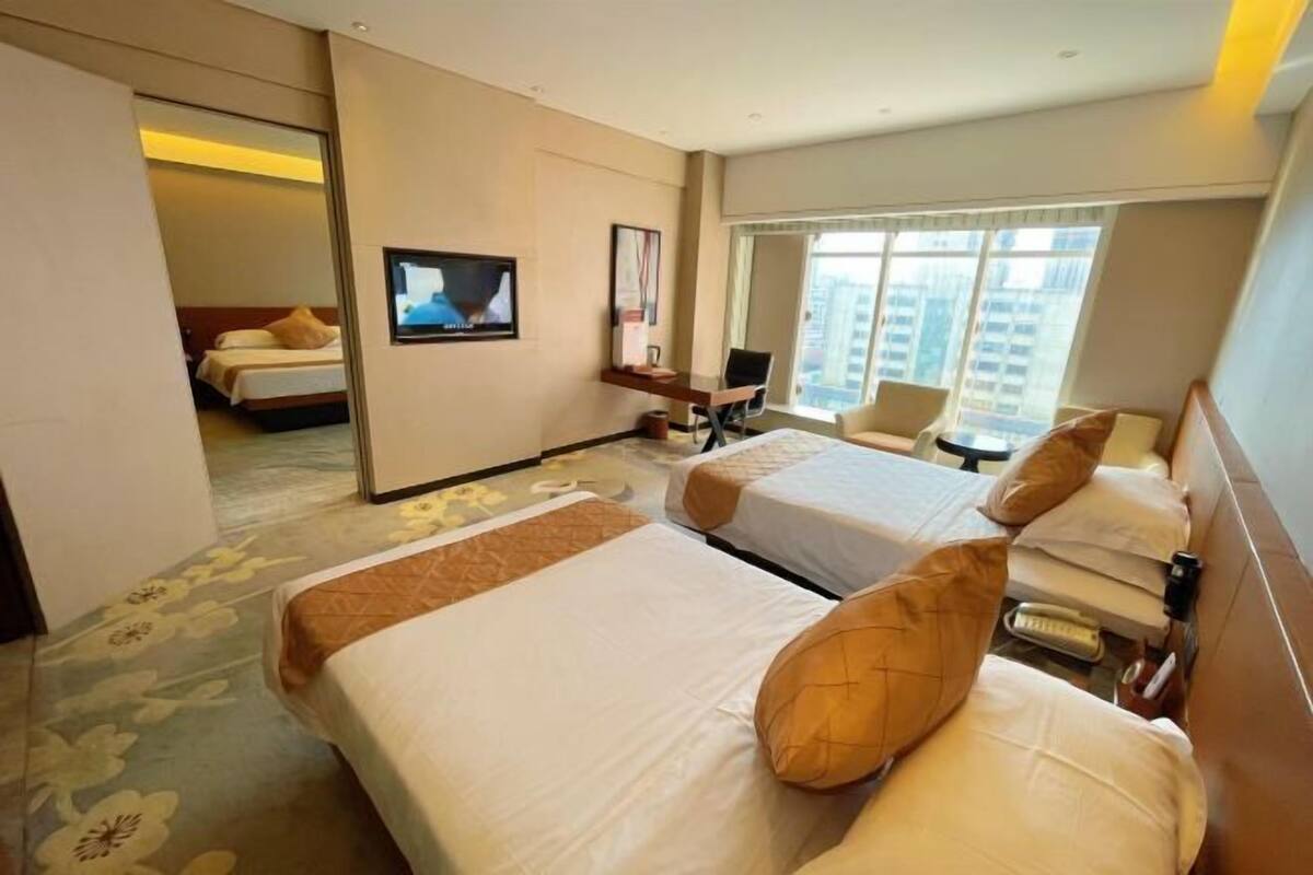 A hotel room with two beds, a TV, a desk, and a large window.