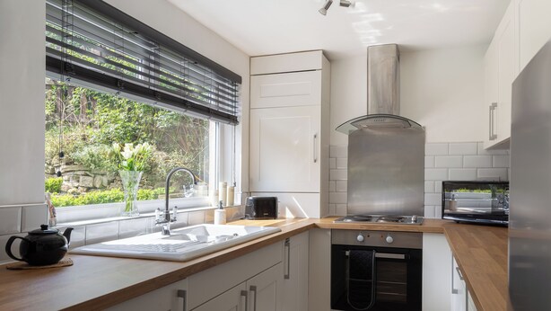 A modern kitchen with a sink, stove, oven, and a window with blinds. - 'Haworth Haven', Warm Winter Cottage Getaway in Yorkshire (Haworth)