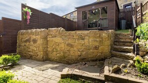 A stone wall with a wooden fence, a stone pathway, and a small garden area with plants. - 'Haworth Haven', Warm Winter Cottage Getaway in Yorkshire (Haworth)