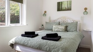 A neatly made bed with a green quilt, two pillows with text, and a forest-themed painting above it. - 'Haworth Haven', Warm Winter Cottage Getaway in Yorkshire (Haworth)