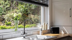 A modern kitchen with a white sink, a black toaster, and a window with a view of greenery. - 'Haworth Haven', Warm Winter Cottage Getaway in Yorkshire (Haworth)