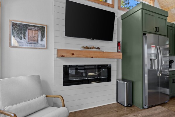 A modern kitchen with a large TV, a built-in oven, and a stainless steel refrigerator.