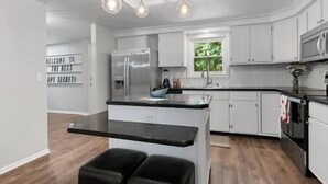 Una cocina moderna con una isla central, muebles blancos y encimera negra.