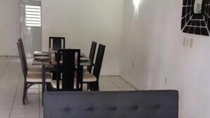 Een woonkamer met een donkergrijze bank, een glazen salontafel met een rode doek, en een eethoek op de achtergrond.