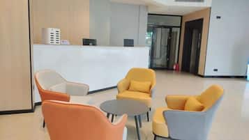Zona de recepción con un mostrador blanco, varias sillas y una puerta de vidrio que da a otra sala.