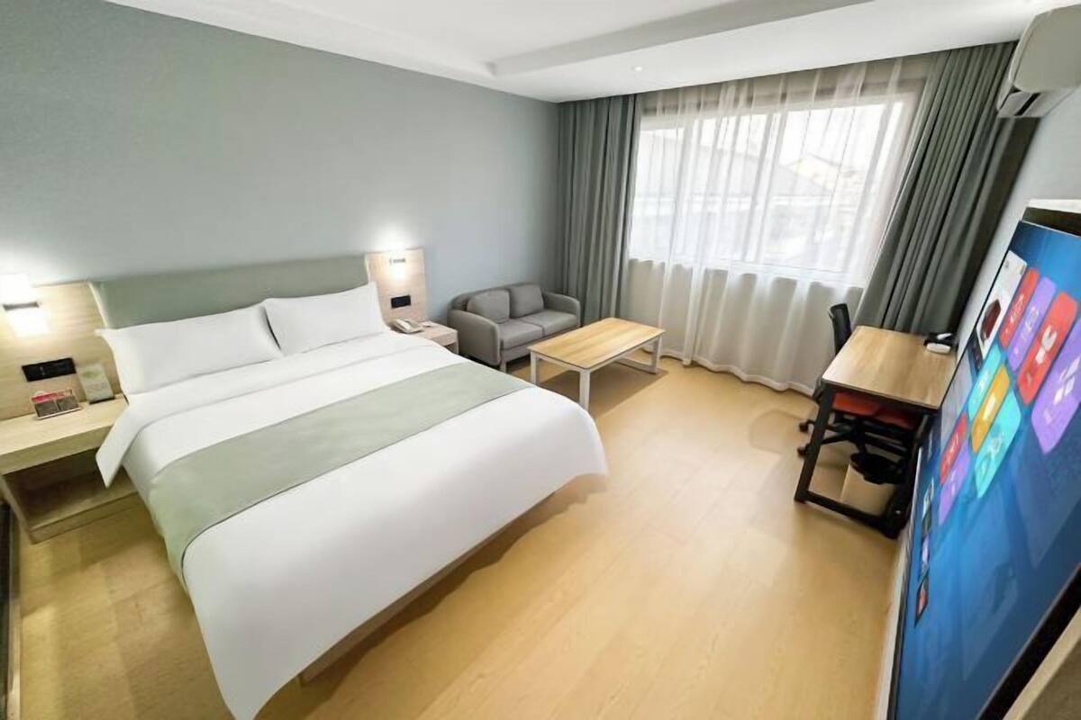 Una habitación de hotel con cama, escritorio, silla, sofá, televisor y cortinas.
