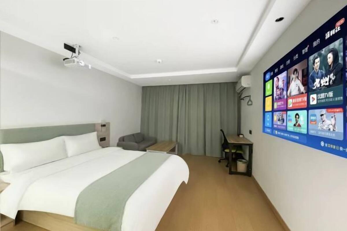 Una habitación de hotel con cama, escritorio, silla, pared con televisor y cortina.