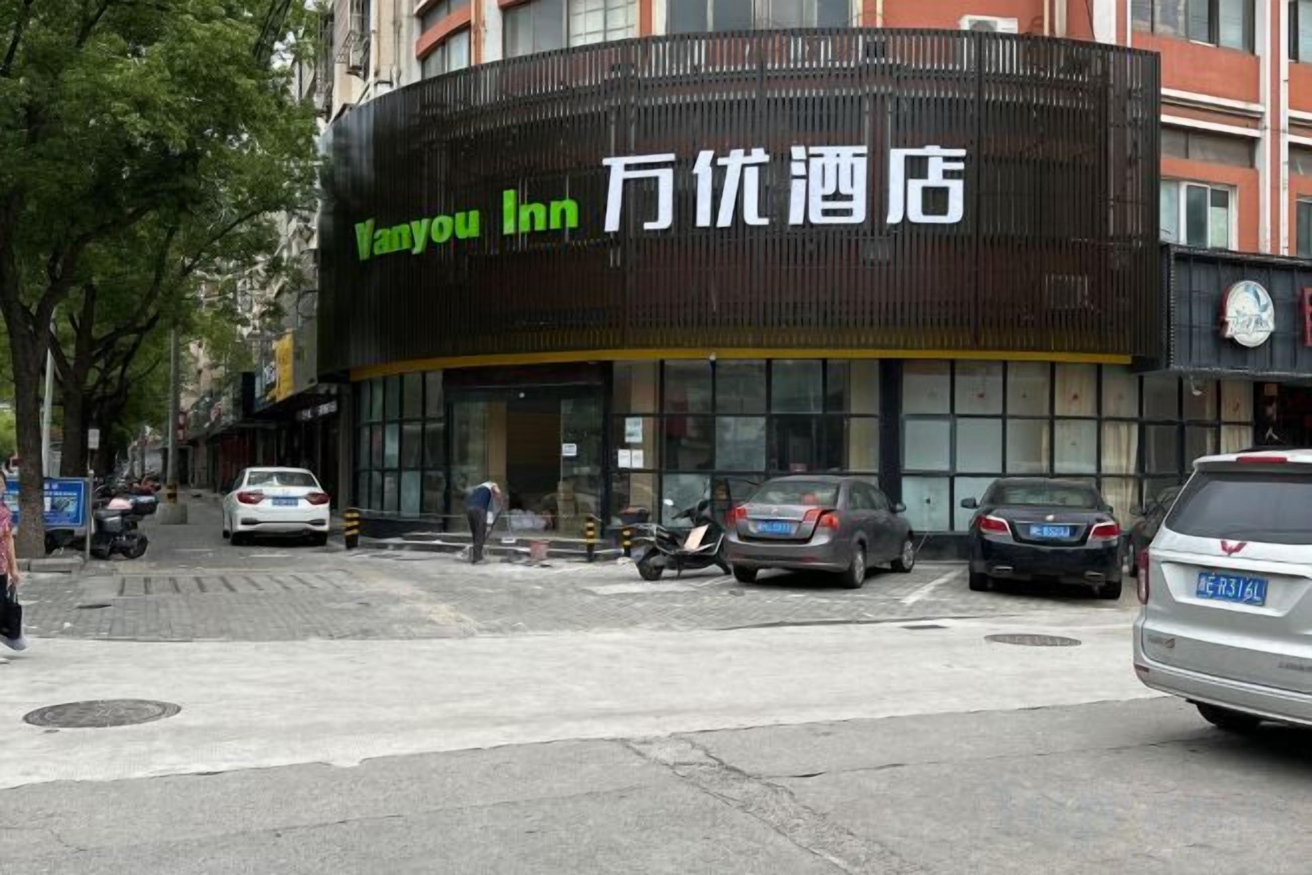 A Vanyou Inn hotel with a modern facade, a visible entrance, and a parking area with cars.