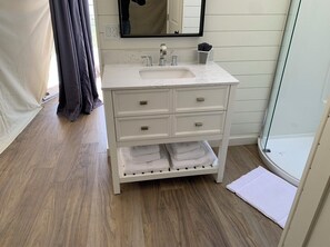 Bathroom features a sink, mirror, drawers, and a shelf with towels.