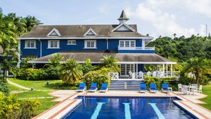 Un edificio azul grande con piscina, rodeado de palmeras y follaje.